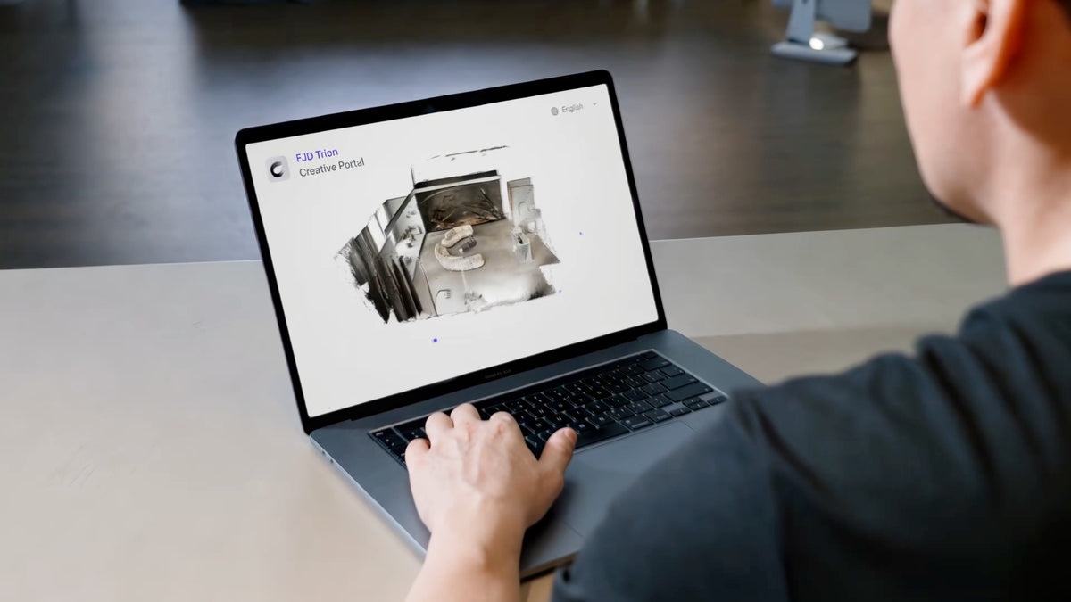 A man working on a laptop in a modern office, the screen displaying the FJD Trion Creative Portal with a 3D point-cloud reconstruction of an interior room.