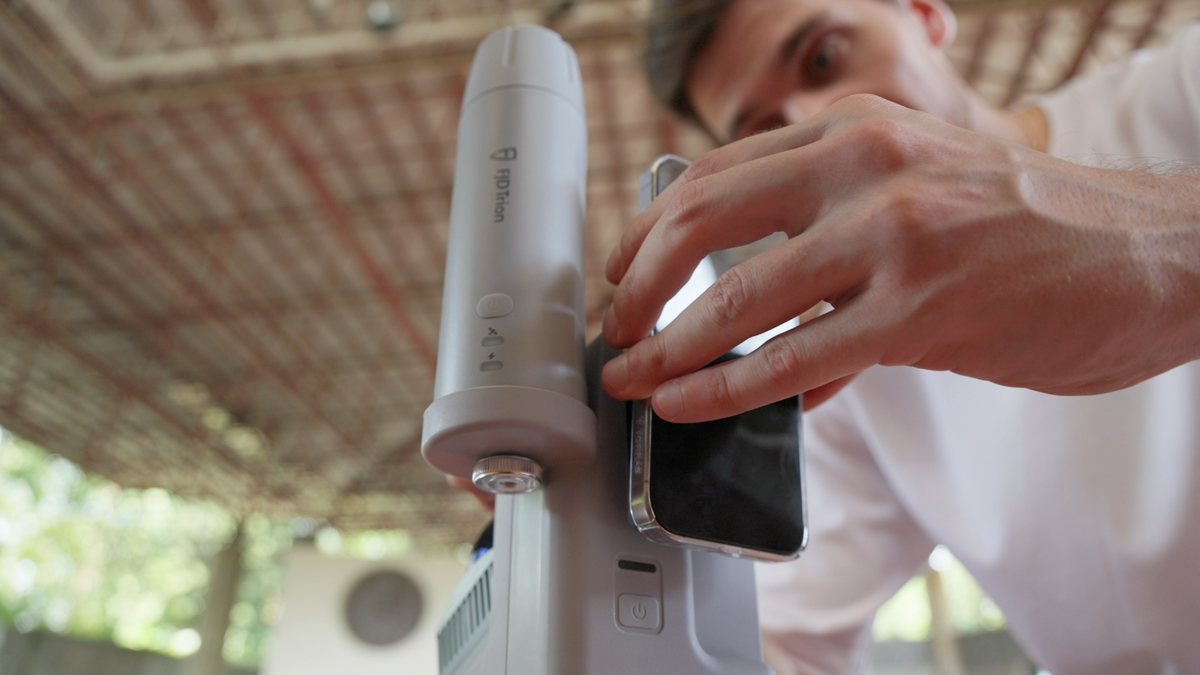 Hands attaching a smartphone to the magnetic quick-release mount of a handheld 3D scanner